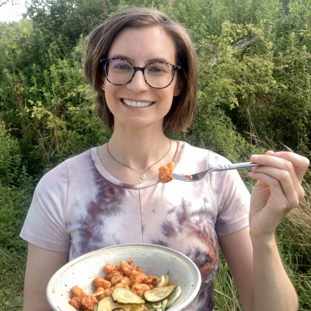 Blog author smiling outside eating a bowl of homemade pasta with red pesto